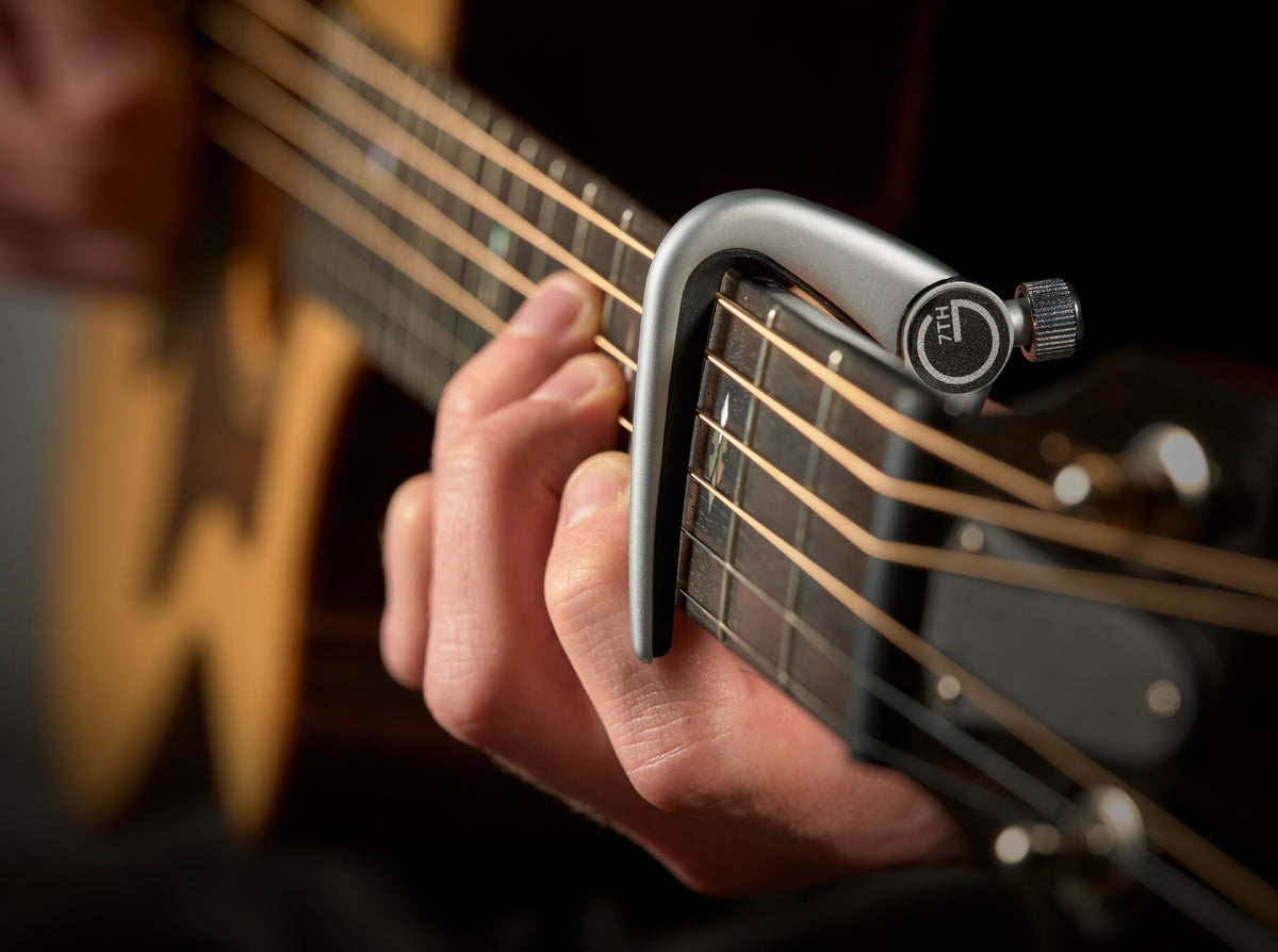 G7th Newport silver capo clamped on an acoustic guitar neck while playing