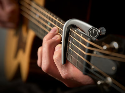 G7th Newport silver capo clamped on an acoustic guitar neck while playing