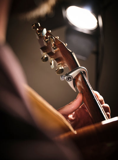Guitarist playing an acoustic guitar with a G7th Newport capo