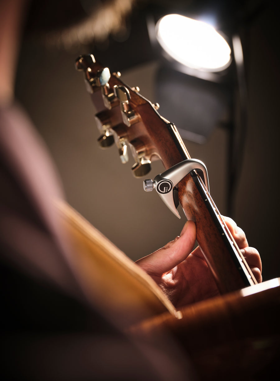 Guitarist playing an acoustic guitar with a G7th Newport capo